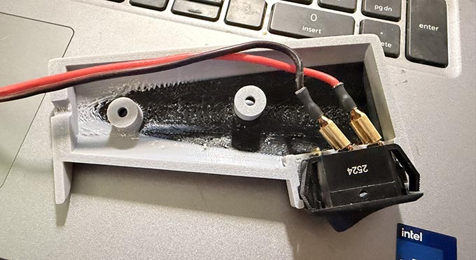 A picture of one half of a 3d printed PTT switch case with the switch and wires laid in place as a mock-up.