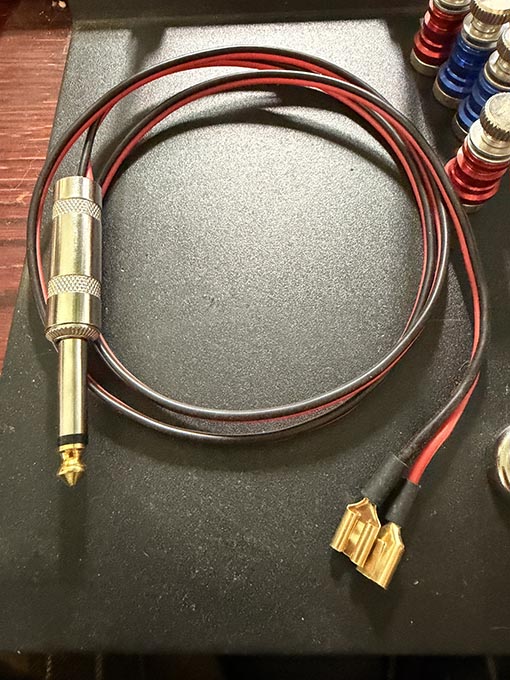 A picture of a coiled length of red & black wiring cable with two gold-colored female spade connectors on one end, and a 1/4" mono audio plug on the other.